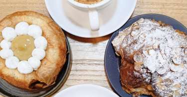 Colazione con cappuccino, croissant alle mandorle e sfogliato moderno con crema e chantilly